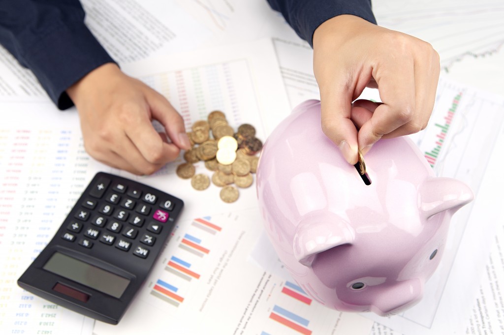 Coin placed inside piggy bank with calculator and papers in the background