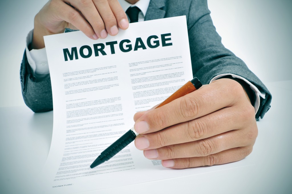 Man wearing a suit sitting in a table showing a mortgage loan contract and where the signer must sign