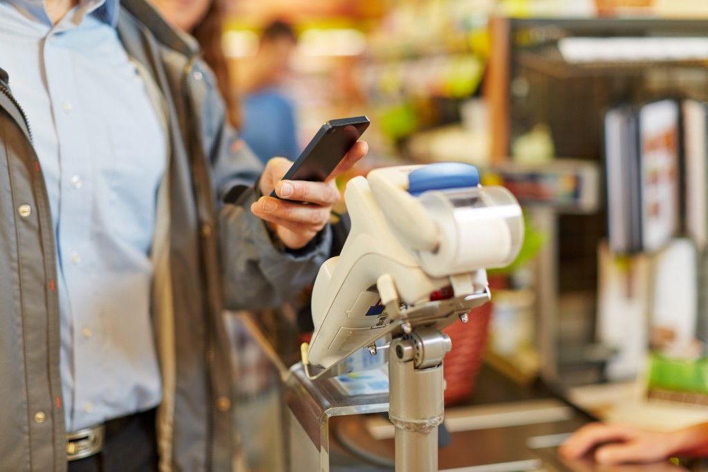 Man paying wireless with his smartphone at supermarket checkout