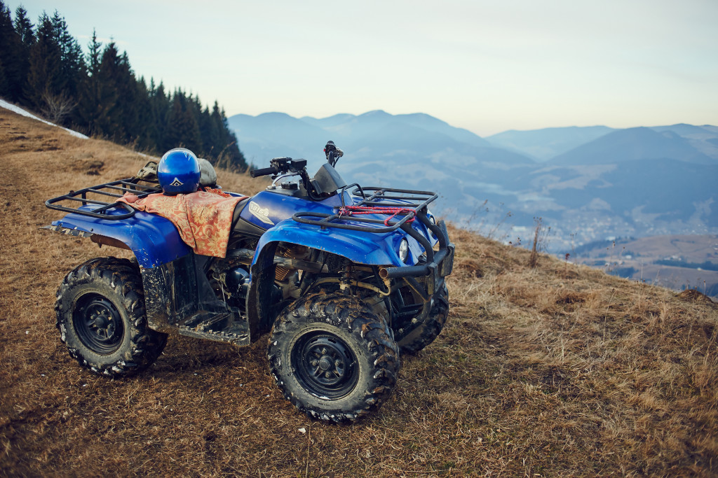 dirty blue ATV parked at the top of a cliff with moutains in the background