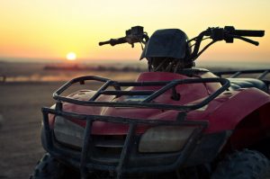 closeup of a dirty red ATV with sun setting in the background